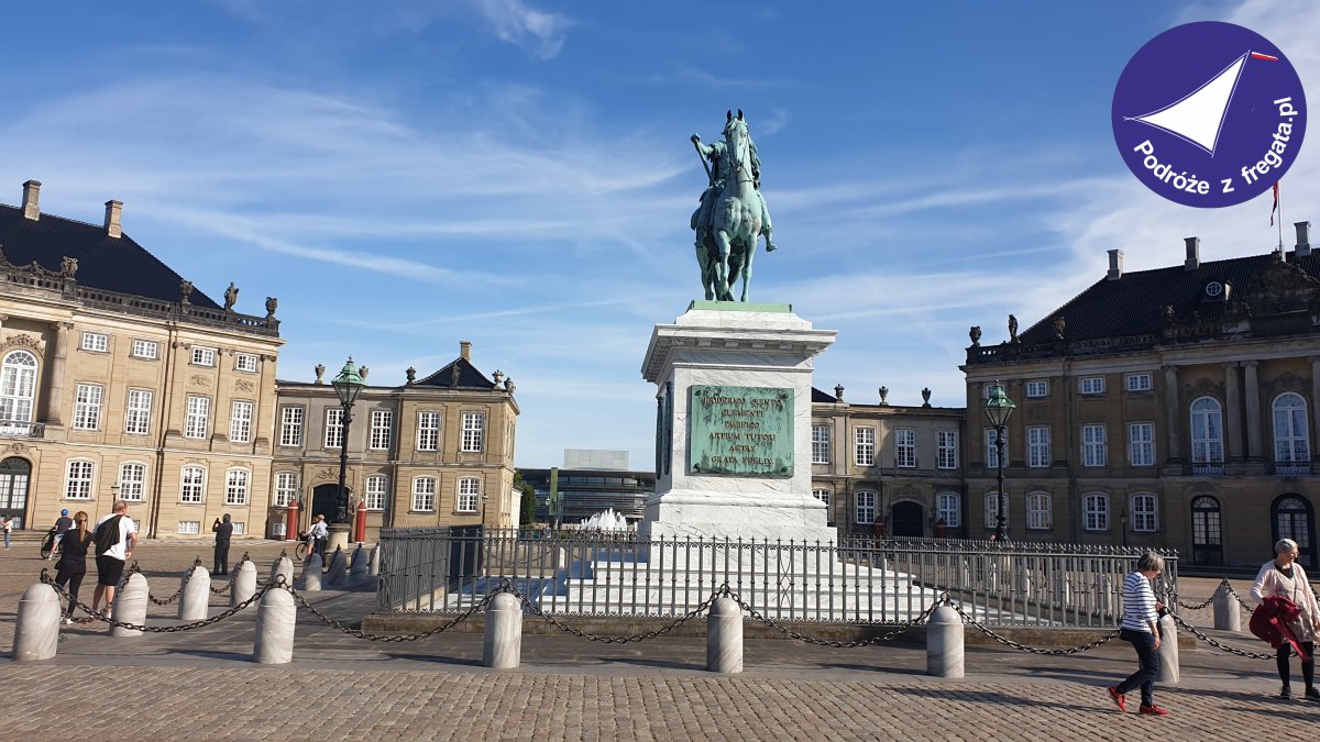 Pomnik konny na placu przed budynkami w Kopenhadze, w tle niebo i spacerujący ludzie.