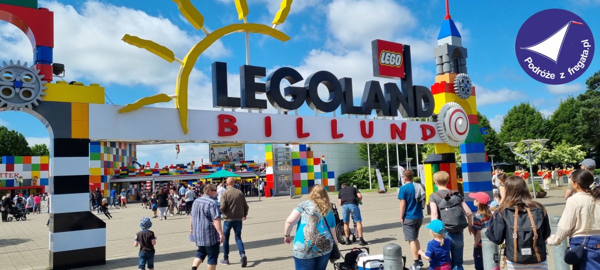 Grupa ludzi przed wejściem do Legolandu w Billund, z kolorowym znakiem i niebieskim niebem.