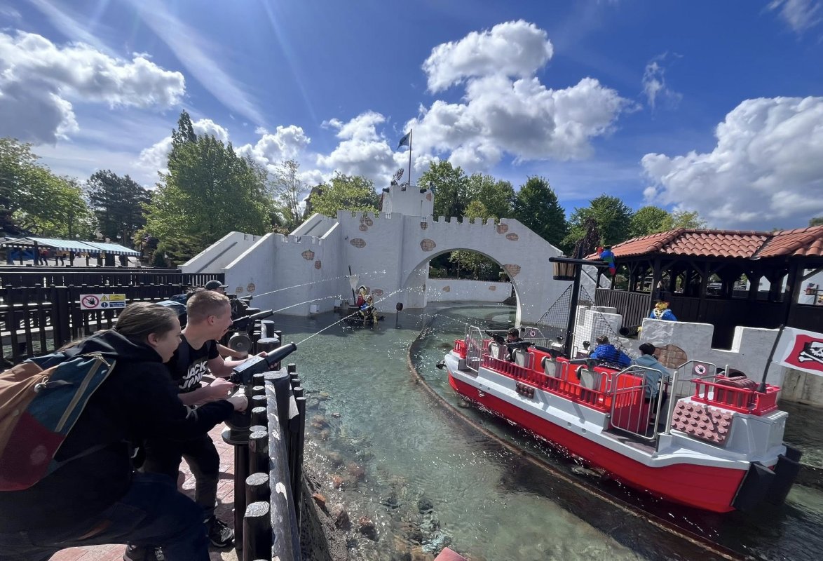 Dzieci bawią się przy wodnym placu zabaw w Legolandzie, w tle zamek i łódź.